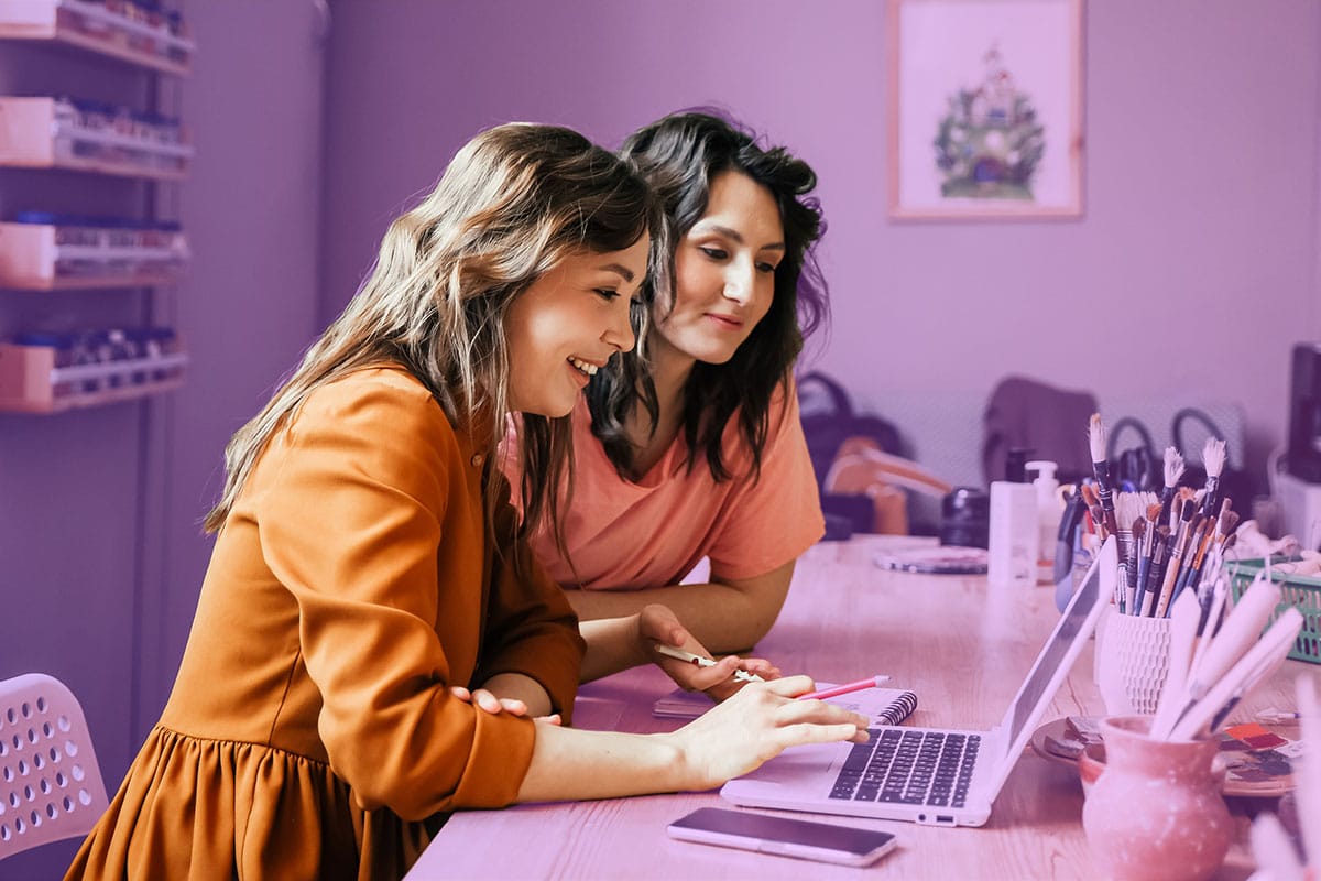 Two women smile while working together on a laptop